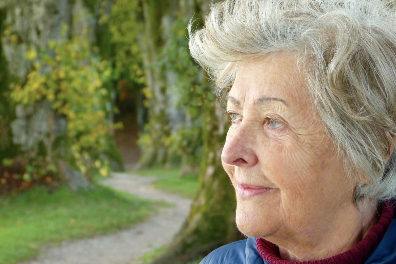 A woman looking into the distance and faintly smiling in a wooded area