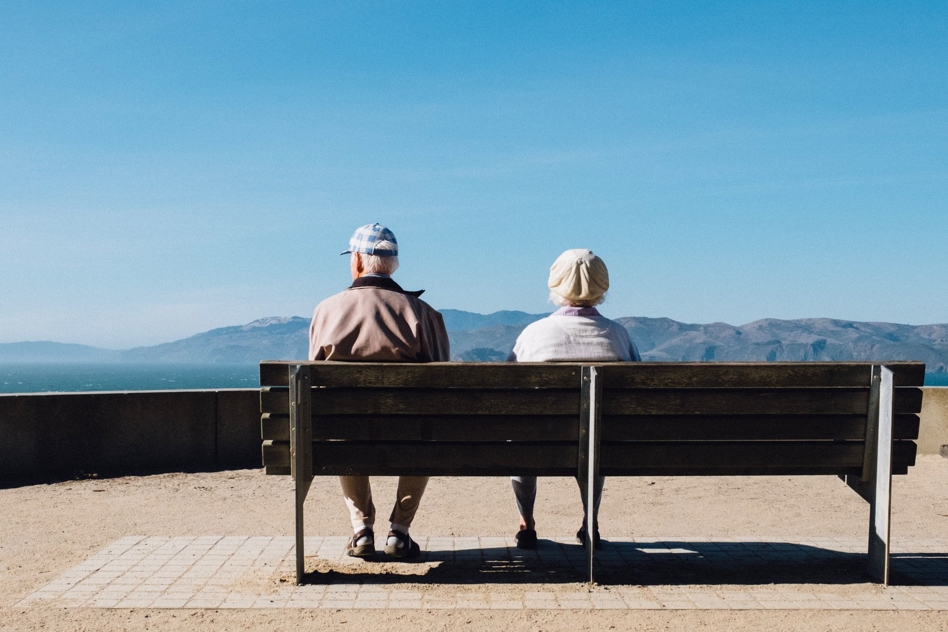Two older people on a bench looking out into the distance over water and mountains