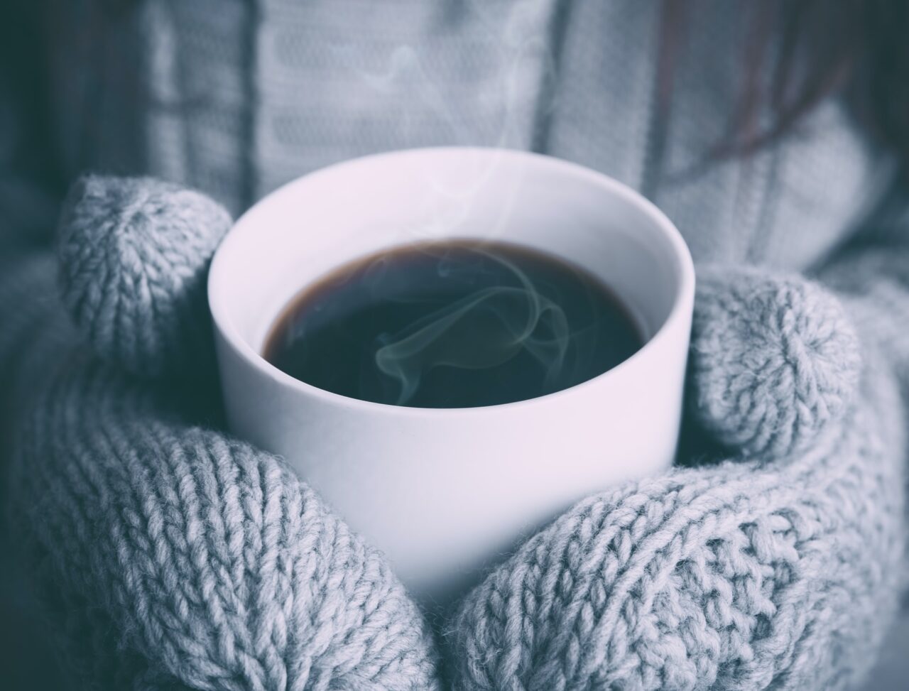 A gloved person holding a mug of coffee