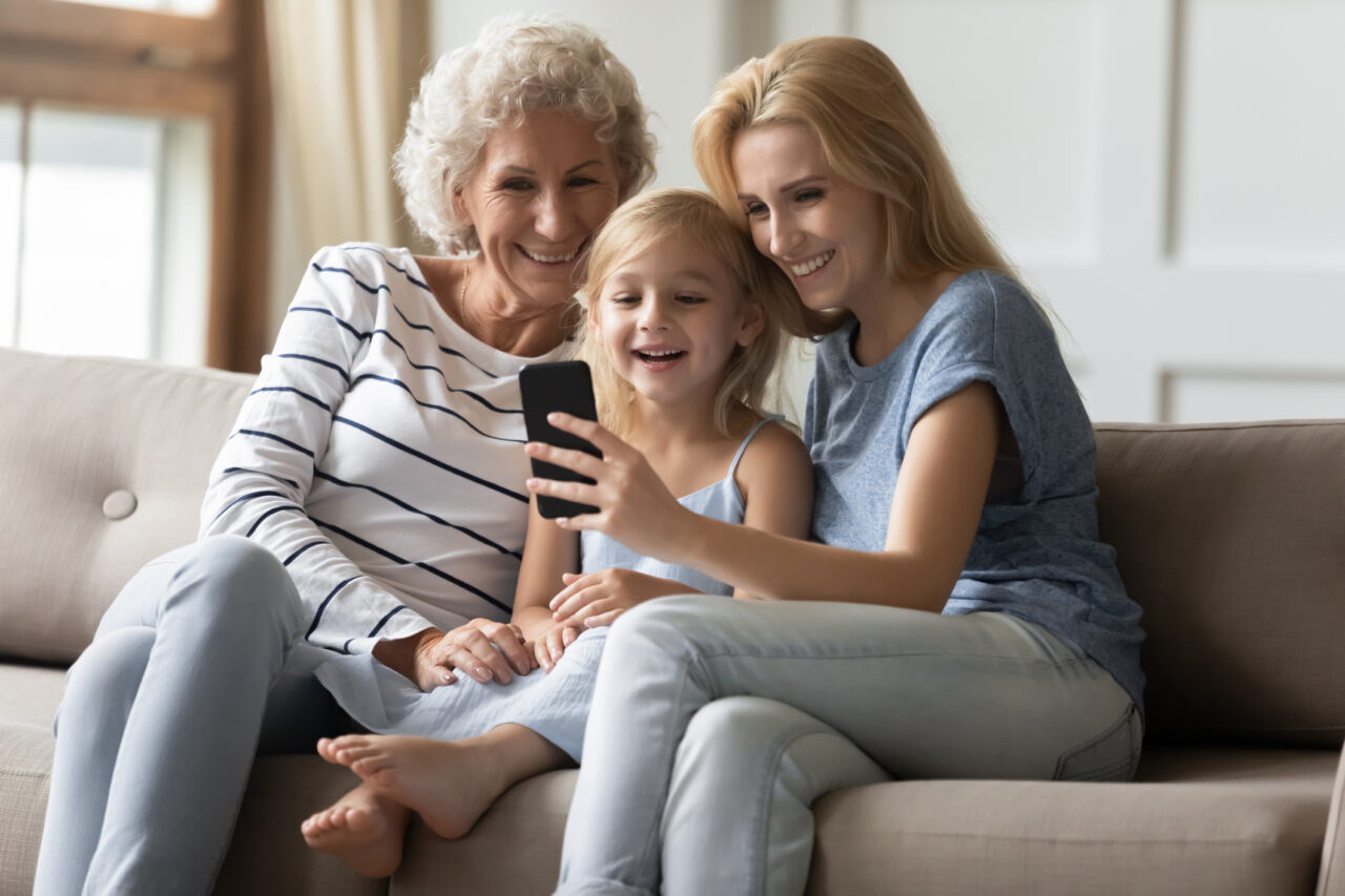 Laughing intergenerational family spending leisure time with smartphone at home