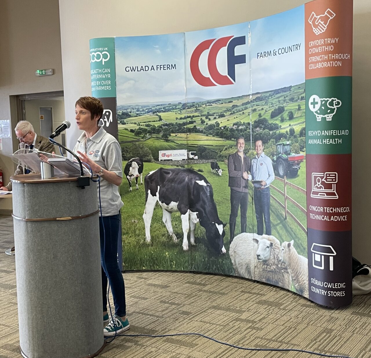 Comisiynydd Pobl Hŷn Cymru, Rhian Bowen-Davies, yn sefyll y tu ôl i ddarllenfa yn siarad yn Sioe Sir Benfro, mewn sesiwn friffio brecwast dan do.