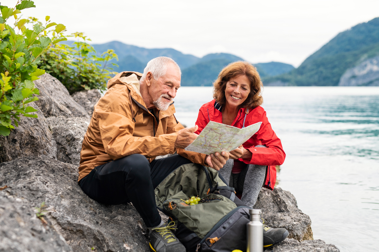Older couple sat on a rock with a lake in the background looking at a map and smiling